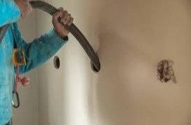 Person using a hole saw to cut a circular hole in a tan wall.