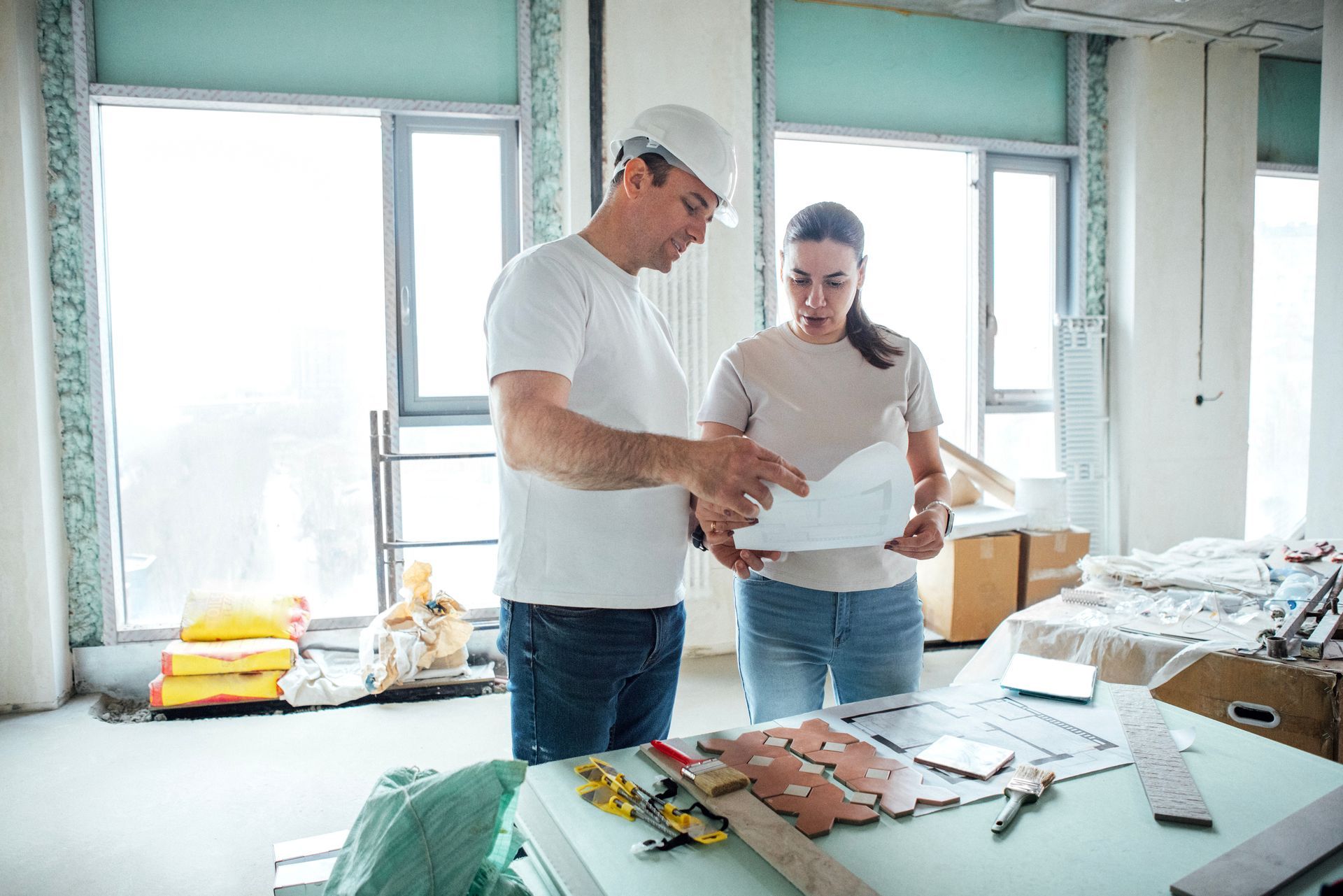 Man in hard hat and woman reviewing blueprints in a construction site with tools on a table. Man in hard hat and woman reviewing blueprints in a construction site with tools on a table.