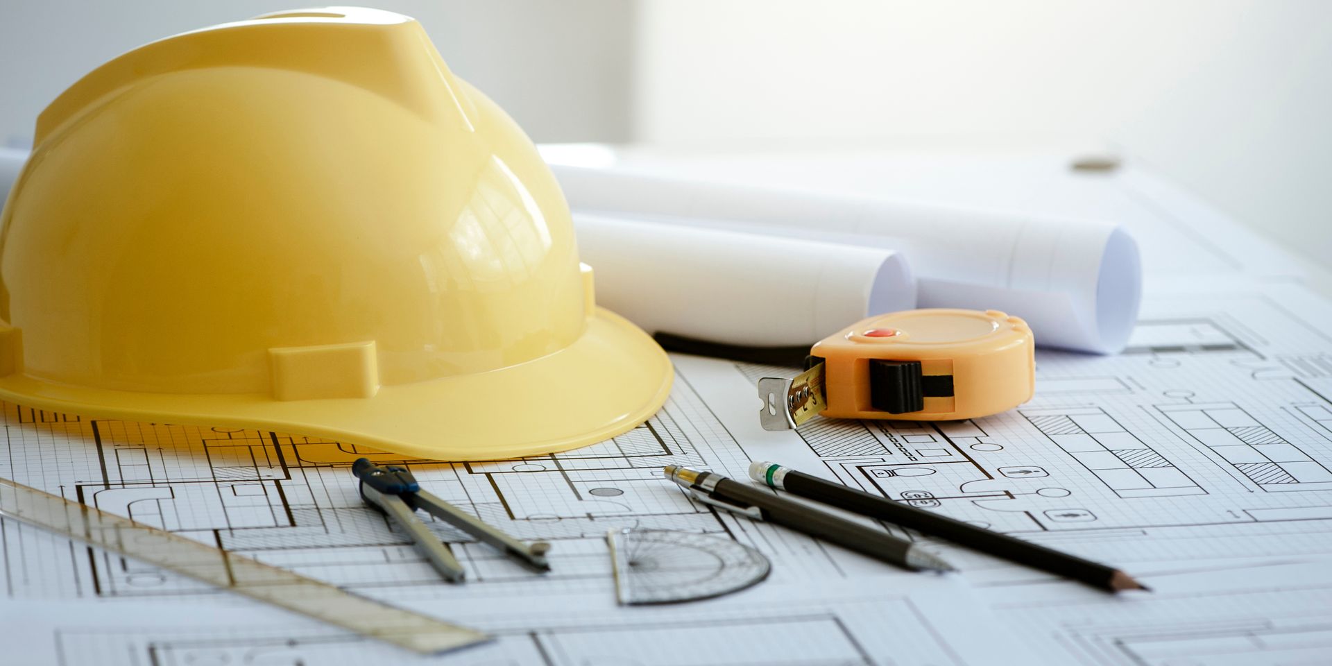 Rolled blueprints, yellow hard hat, and measuring tools on architectural plans Rolled blueprints, yellow hard hat, and measuring tools on architectural plans