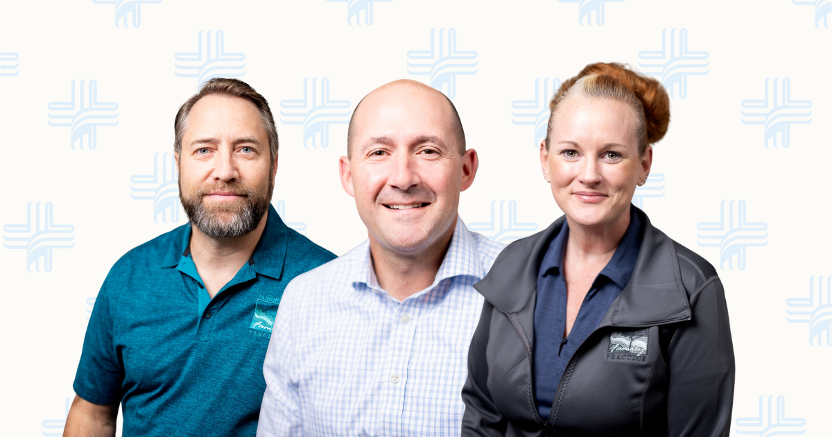 Three smiling coworkers standing side by side against a light patterned background.