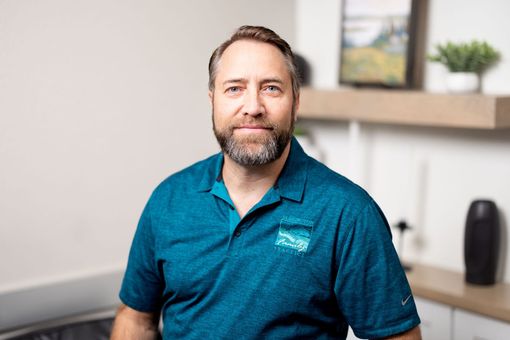 Jonathan Kelly, PA-C in teal polo sitting indoors in a bright office, smiling at the camera.