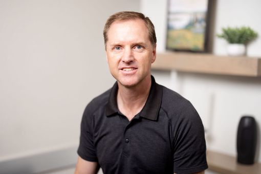 Lance Harmon, MD in a black polo seated in an office, facing the camera with a neutral expression.