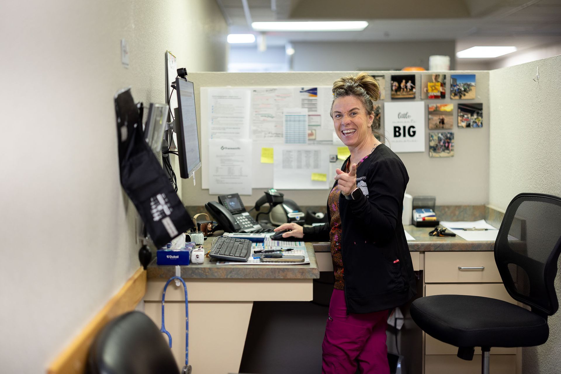 Person smiling in an office cubicle, holding up a peace sign near a desk and chair.