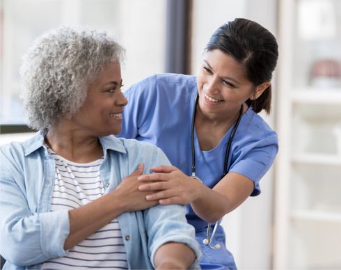 Nurse in blue scrubs gently comforts a smiling patient in a bright room