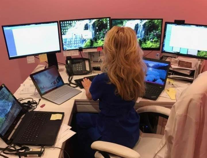 A woman is sitting at a desk with multiple monitors and laptops