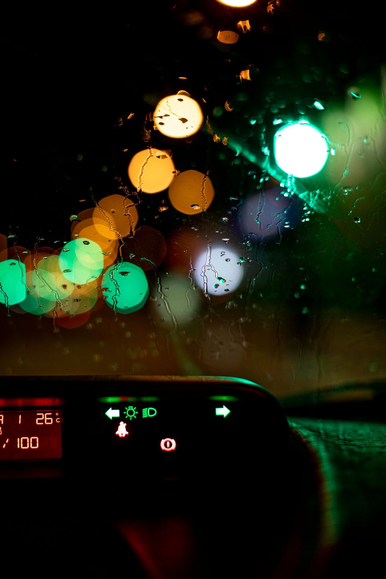 Driving at night, lights blurred. Rain on windshield. Dashboard lights illuminated.
