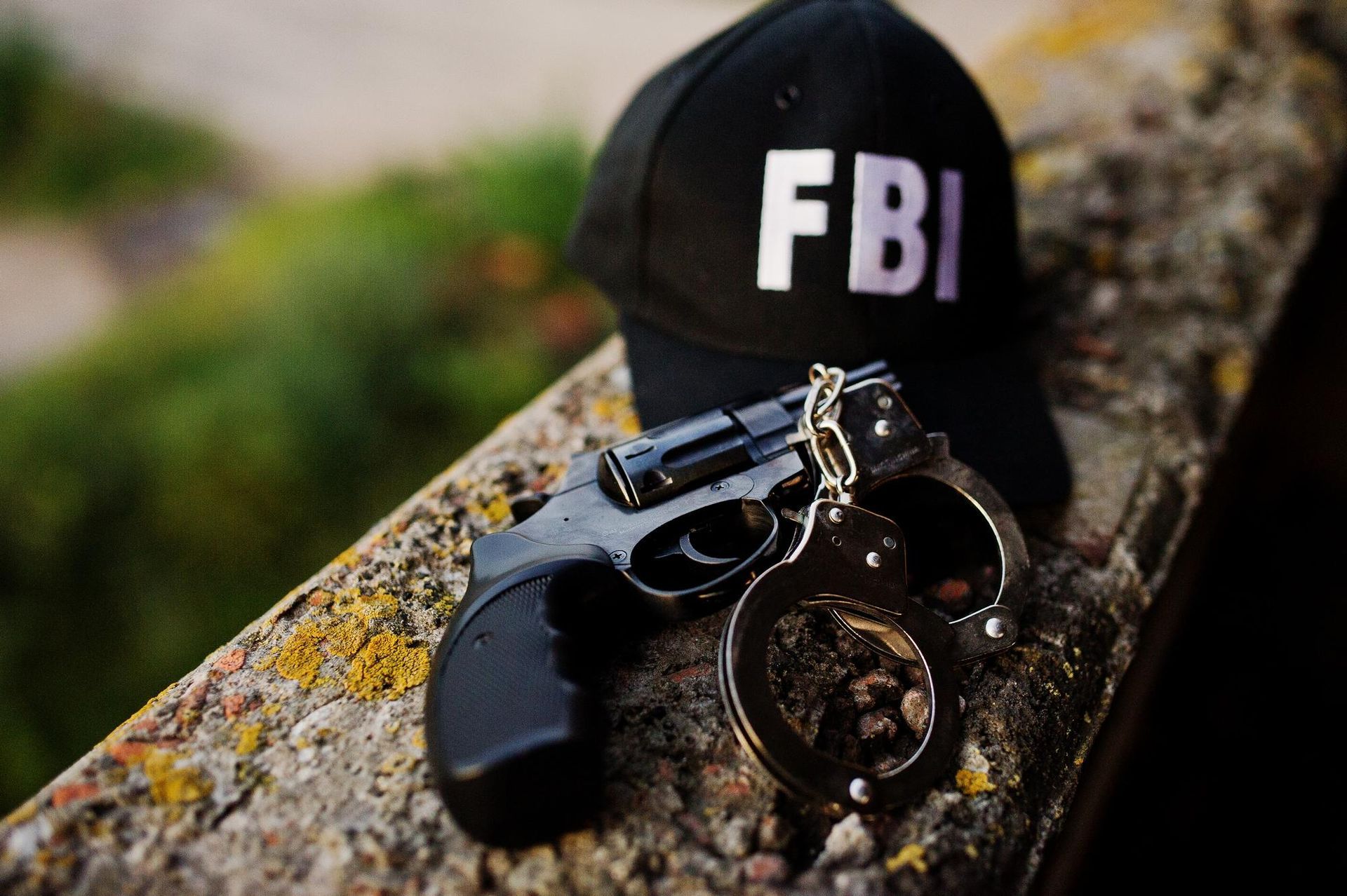 Black handgun, handcuffs, and FBI hat on a stone surface, blurred background. 