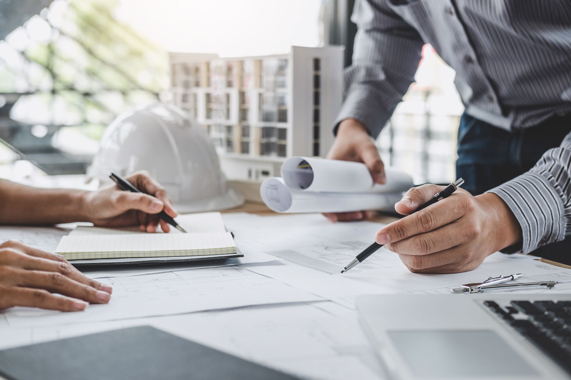 Two architects reviewing blueprints at a desk with a model building. 