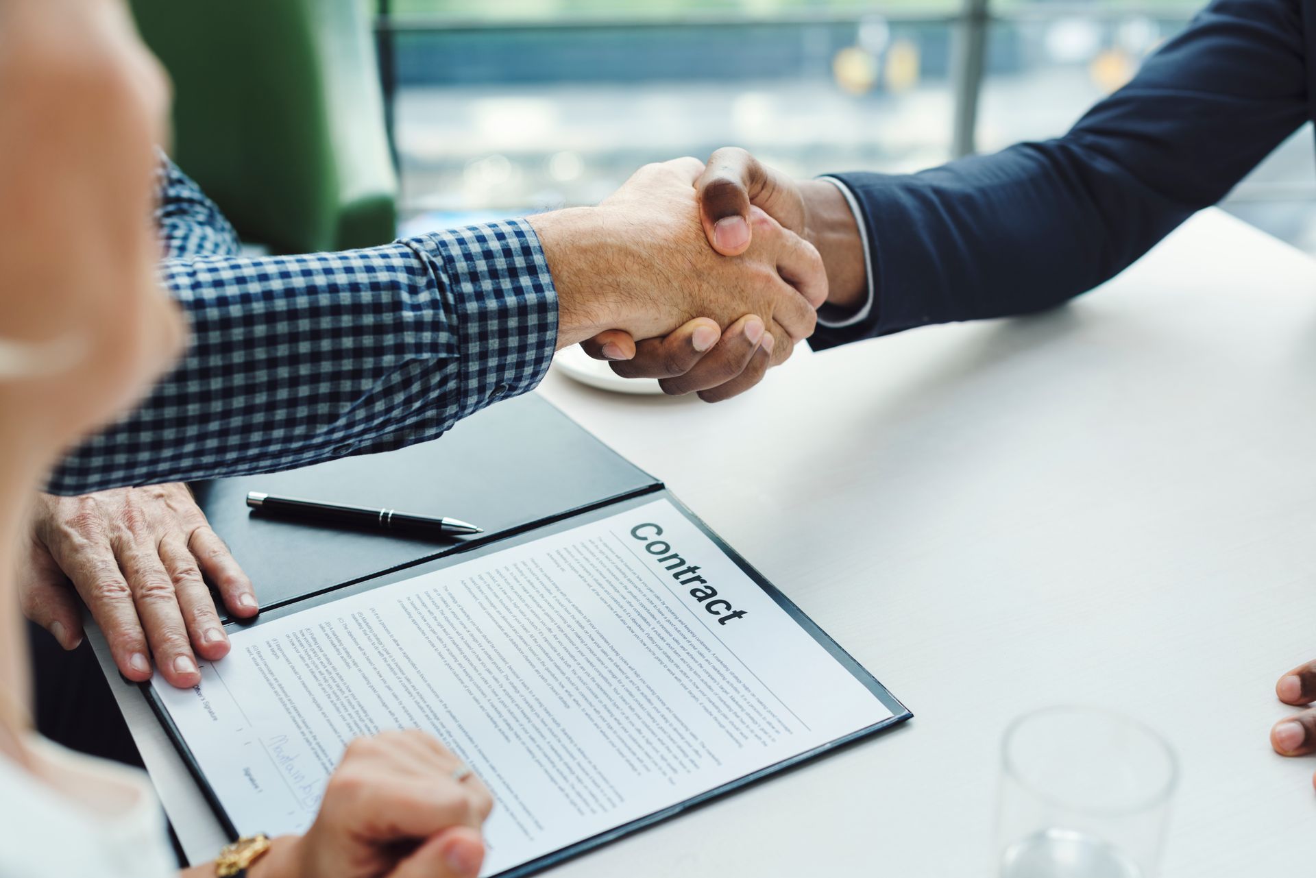 Two men shaking hands over a contract on a table, symbolizing an agreement. 