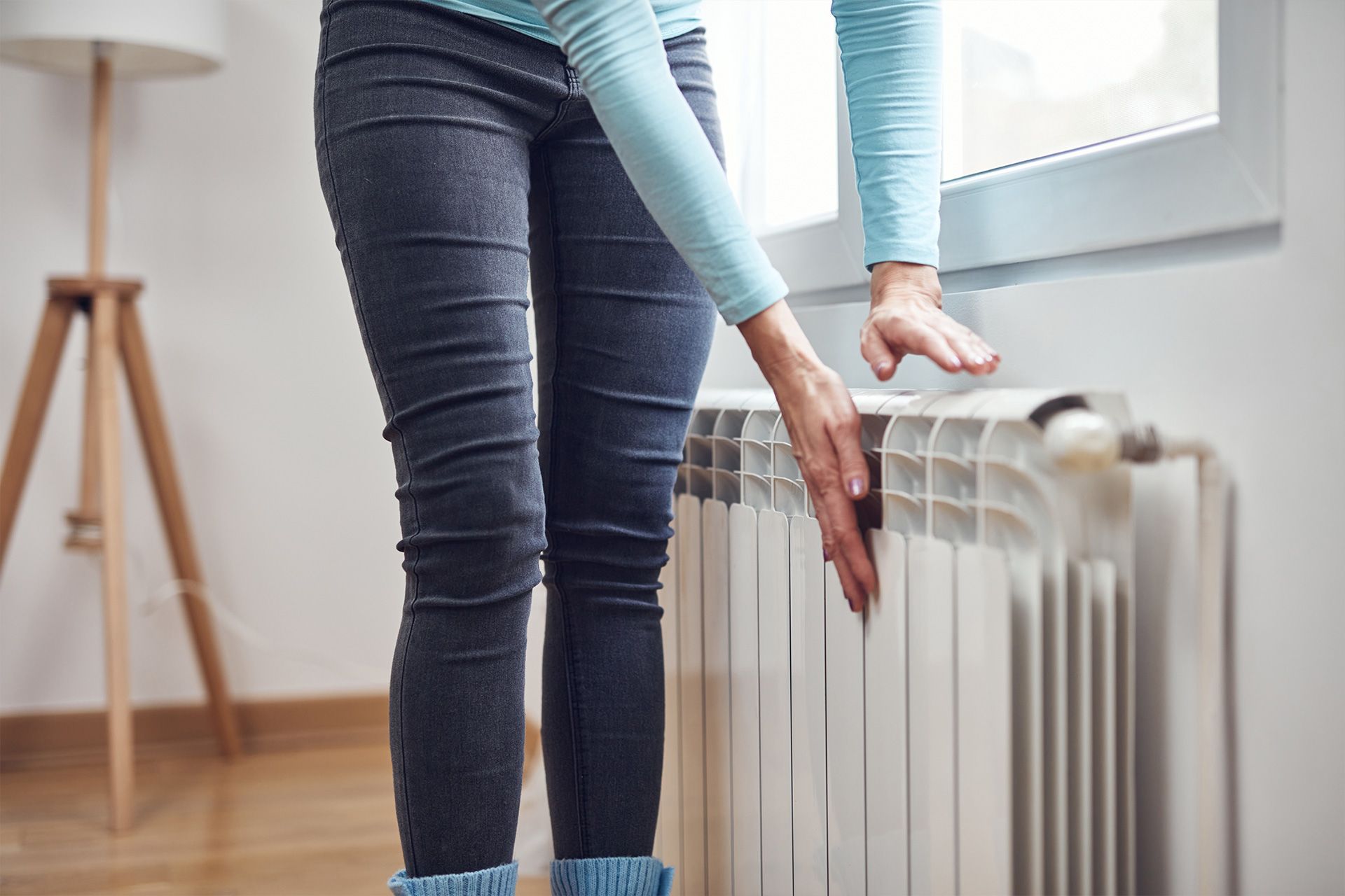 A woman is standing next to a radiator in a living room.Emergency AC Repair & Services