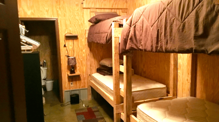 Wood-paneled bunk room with bunk beds, shelves, and a small doorway in the back.