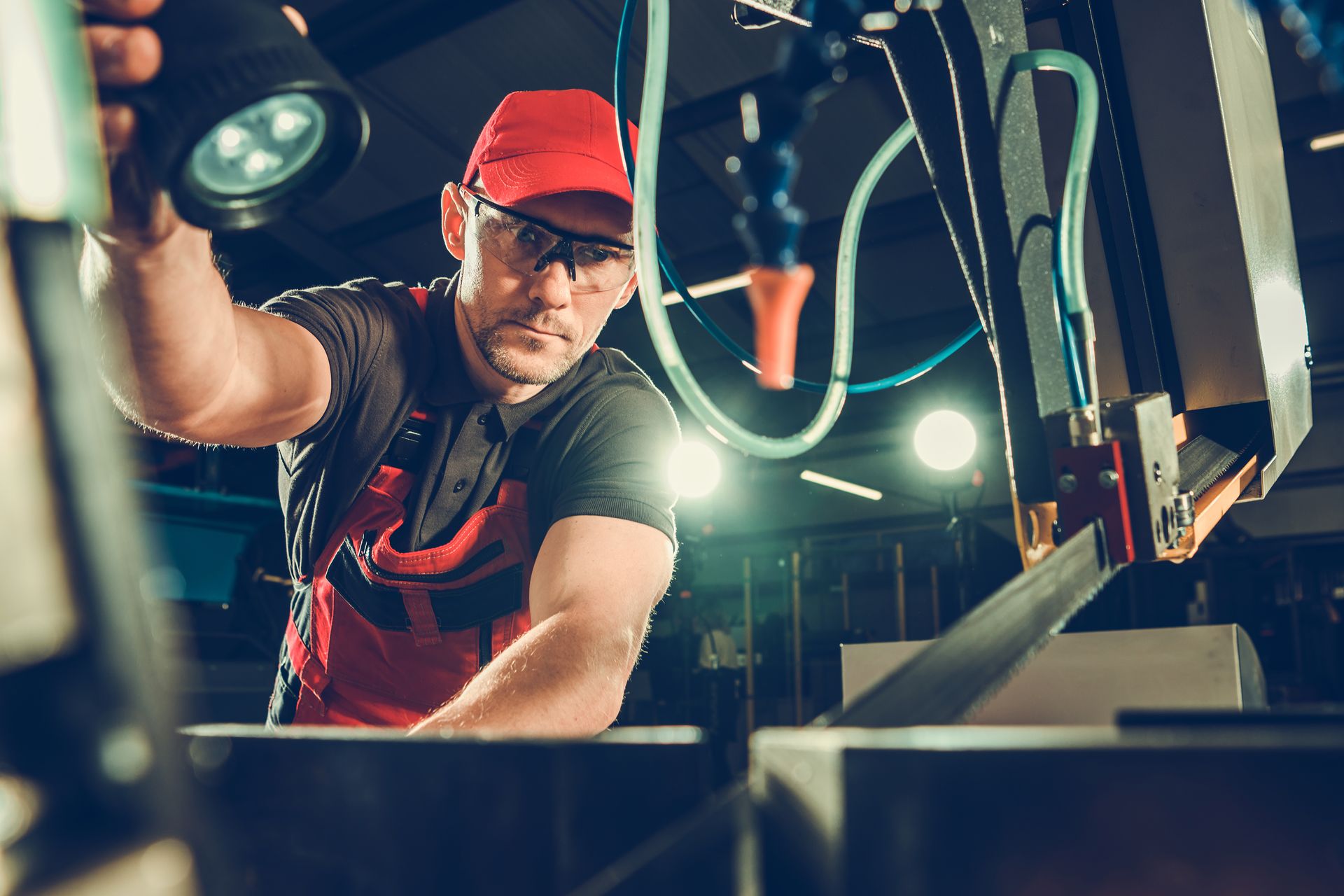 A man is working on a machine in a factory while holding a flashlight.