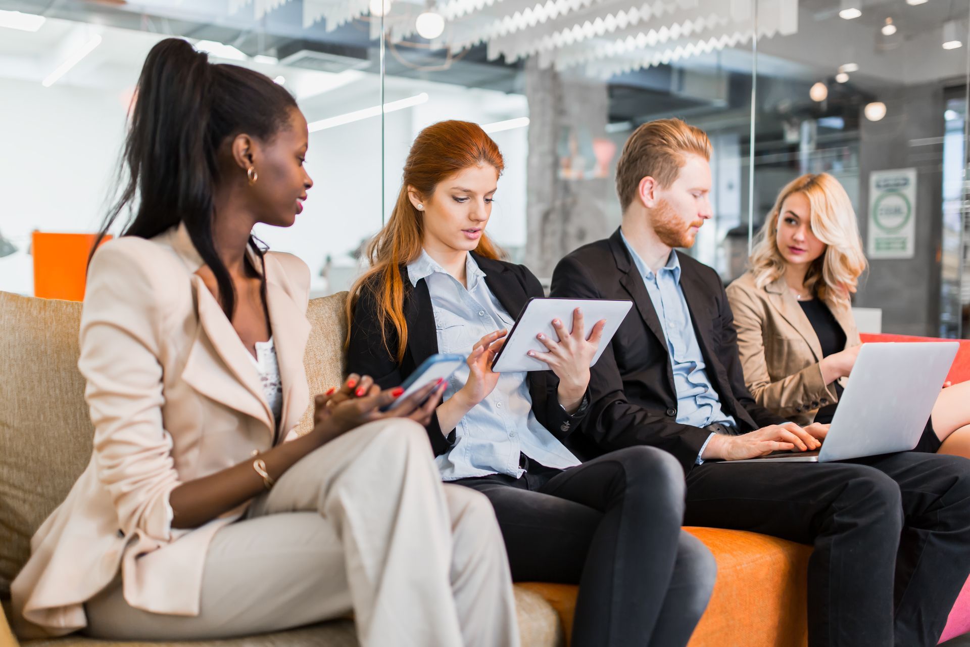 A group of people are sitting on a couch with laptops and tablets.
