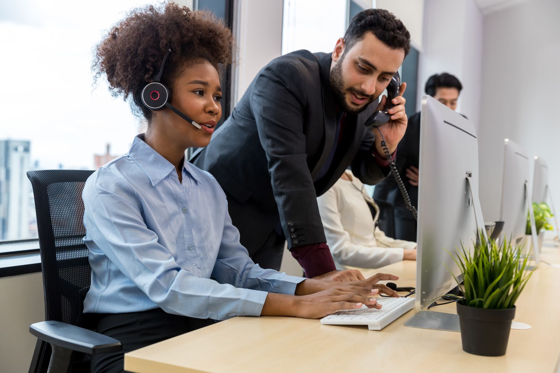 A man is talking on a cell phone while a woman looks at a computer screen.