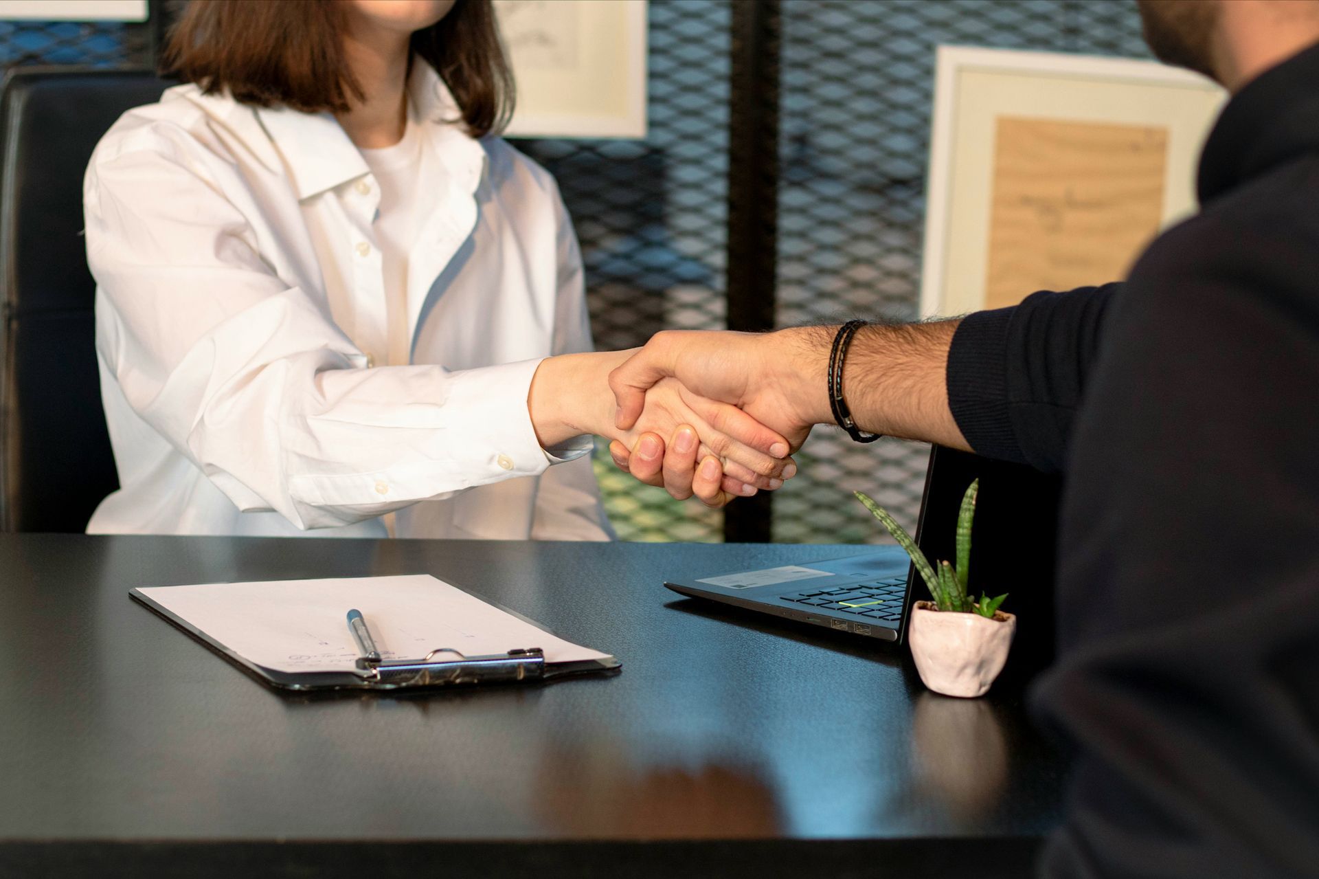 A man and woman doing a handshake on an office table.
