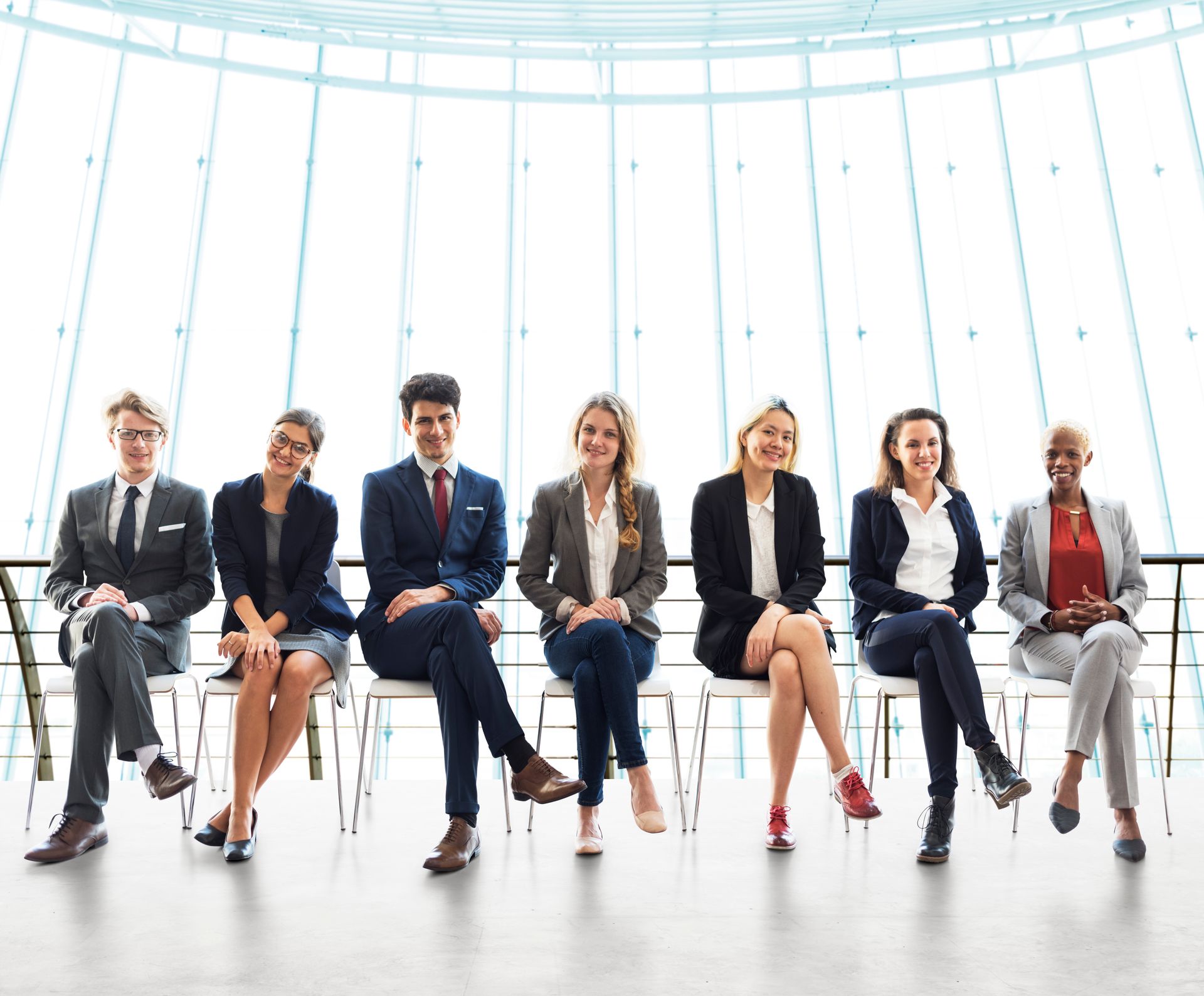 A group of business people are sitting in a row in front of a large window.