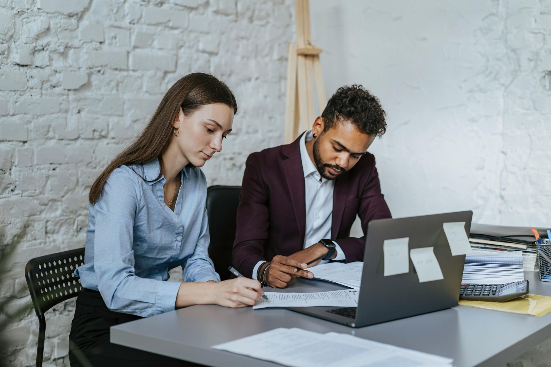 A man and a woman are sitting at a table looking at a laptop.
