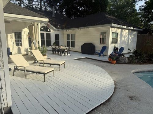 Backyard patio with white deck, lounge chairs, table, and a pool beside a cream-colored house