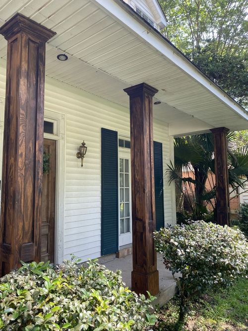 Front porch with white siding, dark wooden columns, and bushes in front of a house.