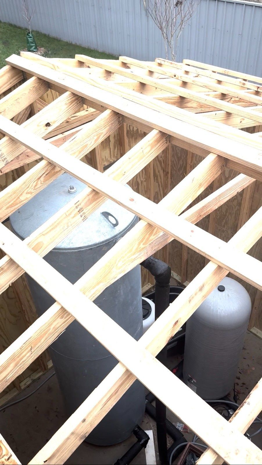 Wooden roof framing over large propane tanks beside a corrugated metal wall