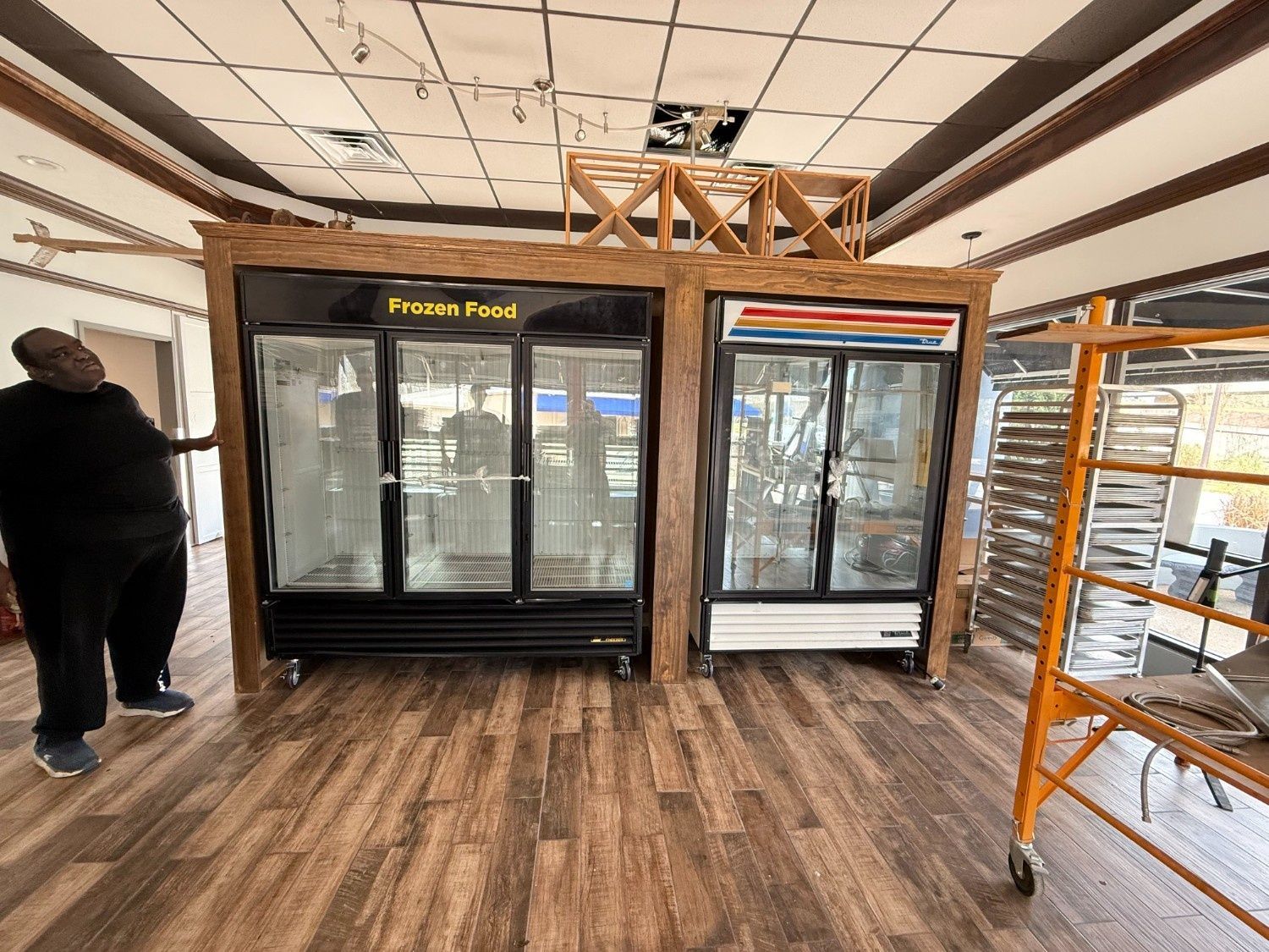 Store interior with glass-door refrigerators and orange shelving on a wood floor