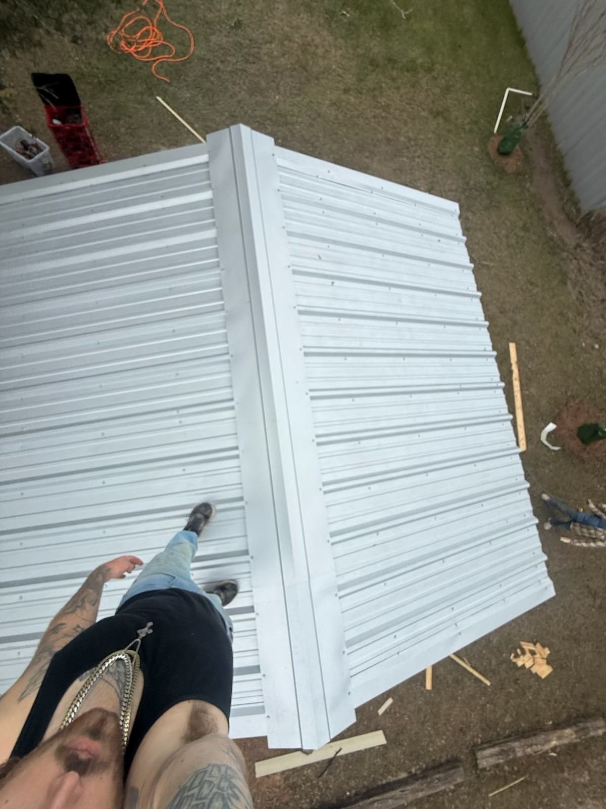 Person standing on stacked white corrugated metal sheets outdoors, viewed from above.