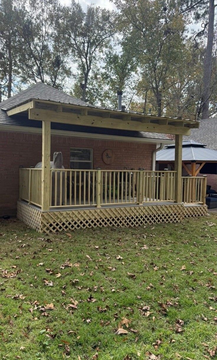 Wooden porch attached to a red brick house, with a lattice skirt and trees in the background.