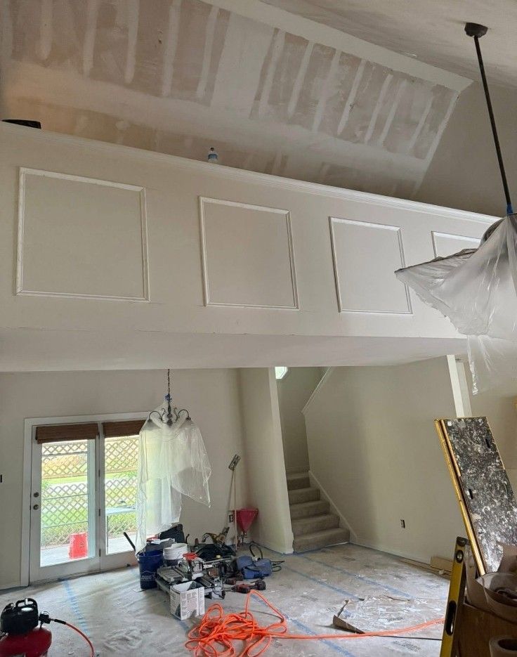 Interior under renovation with white walls, a staircase, hanging light fixture, and construction materials on the floor