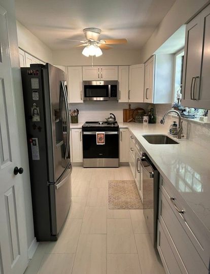 Bright narrow galley kitchen with white cabinets, stainless appliances, and light wood floors