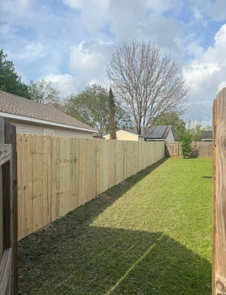 Narrow grassy backyard bordered by wooden fences under a partly cloudy sky.