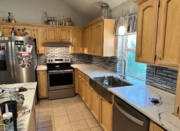 Bright kitchen with wooden cabinets, stainless appliances, tiled floor, and window over the sink