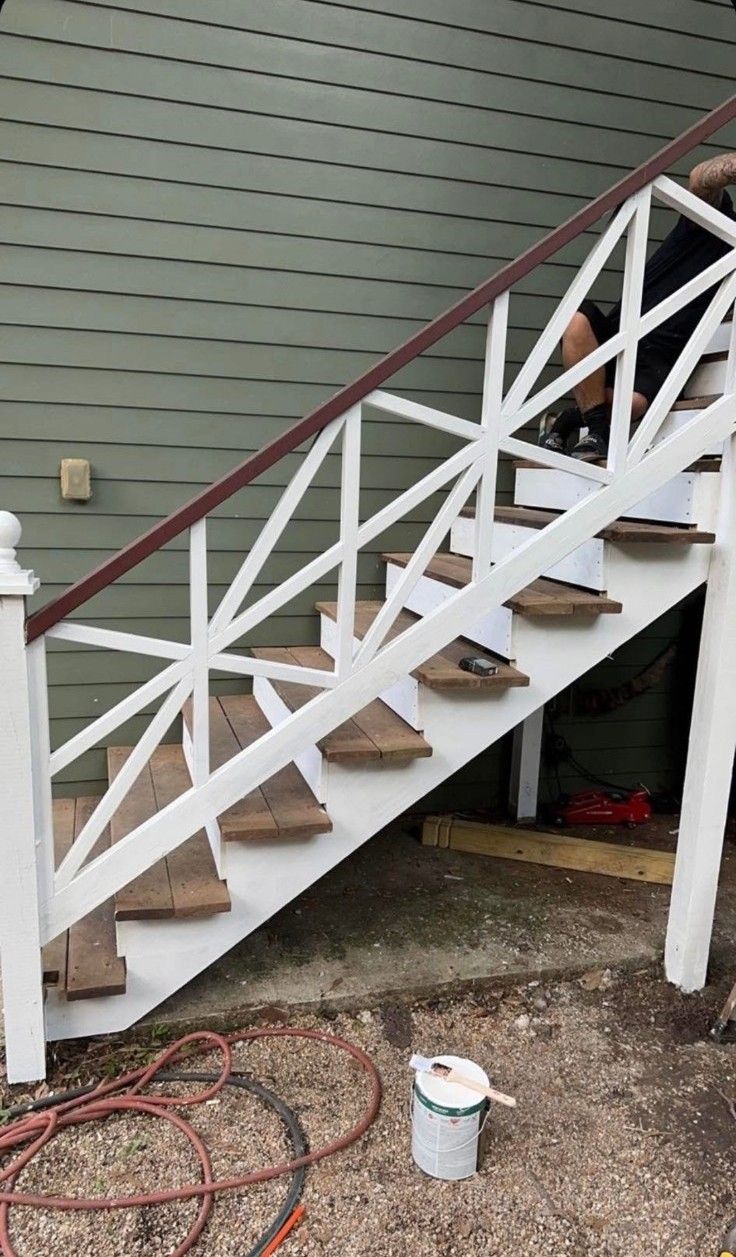 White wooden outdoor staircase with brown handrail beside gray siding, under construction with tools below