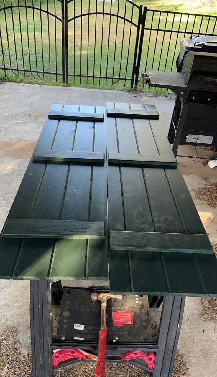 Green painted wooden tabletop on a patio, with a grill and fence in the background.