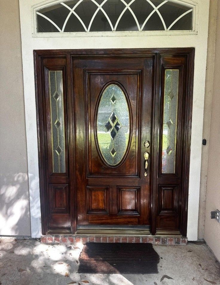 Dark wooden front door with oval glass panel and sidelights, framed by a light stucco entryway.