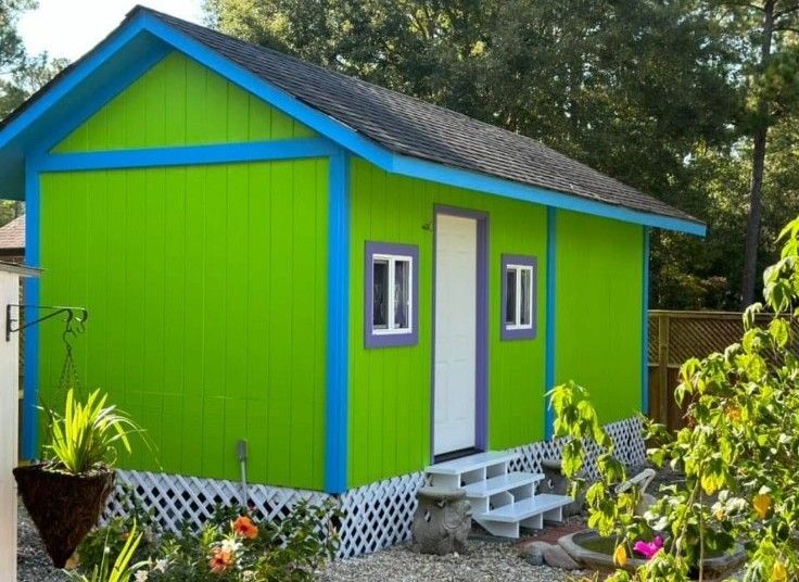 Small lime-green shed with blue trim and white door in a garden setting.