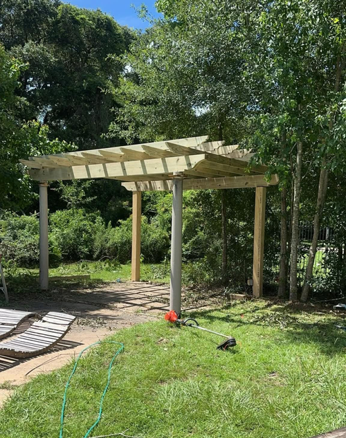 Wooden pergola in a sunny garden beside trees and grass