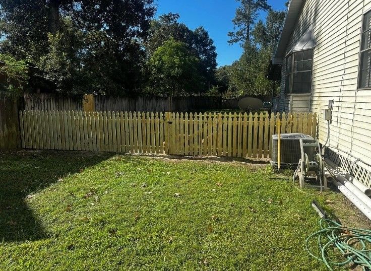 Backyard with green lawn, wooden fence, trees, and the side of a house with a hose reel