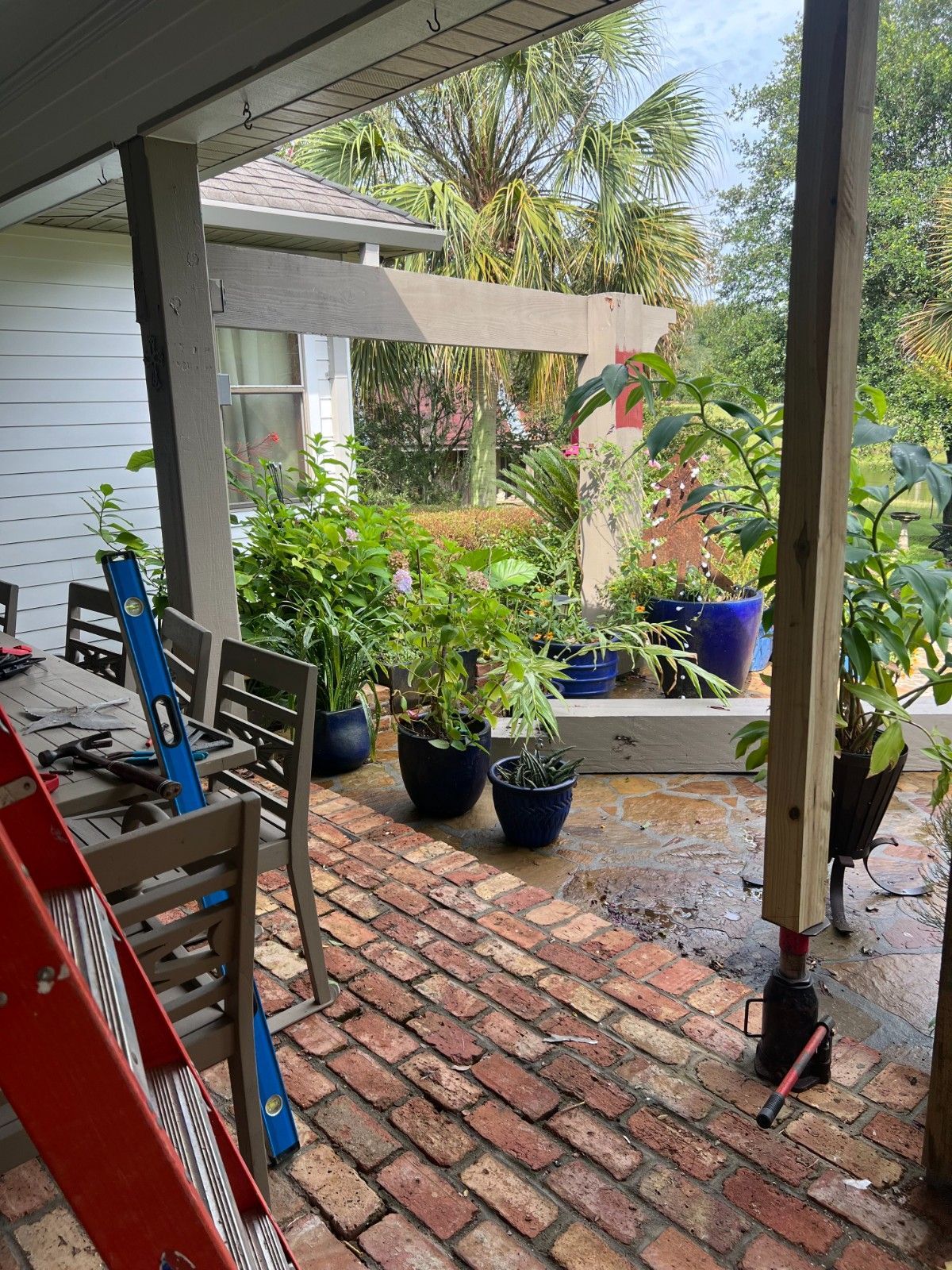 Porch with red brick floor, potted plants, and colorful chairs overlooking a leafy garden
