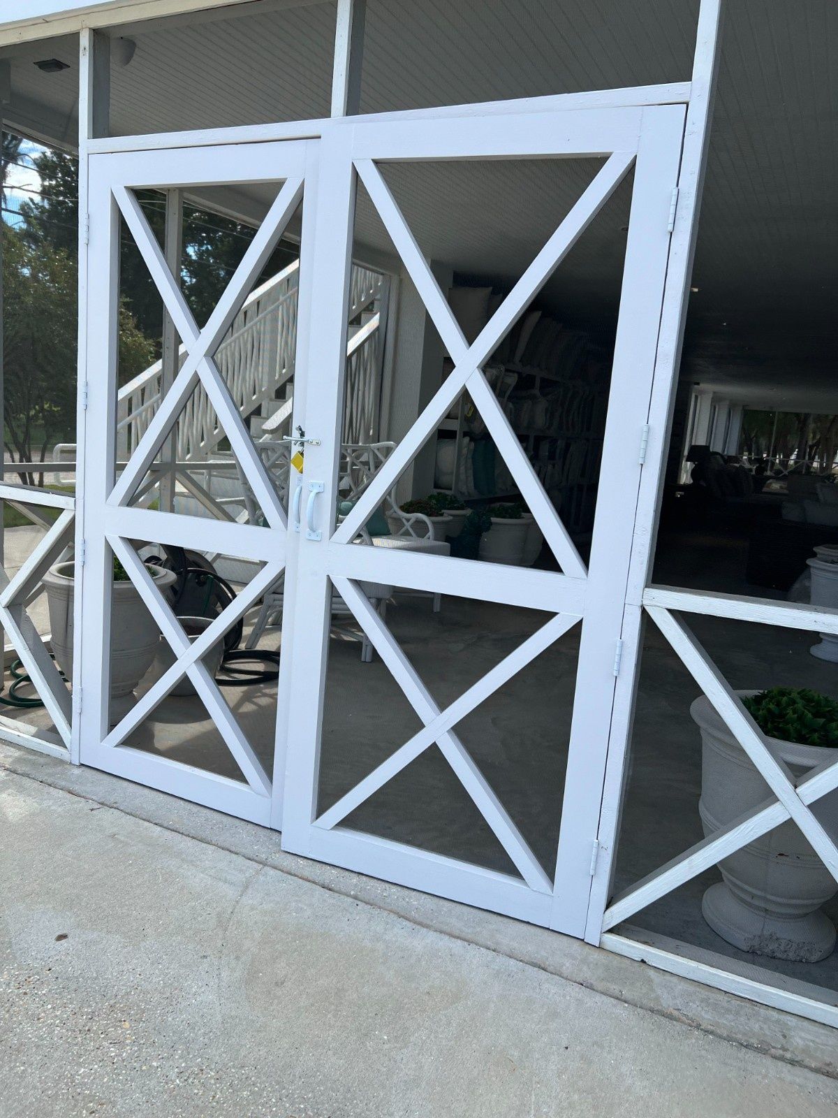 White X-braced gate panels beside a windowed building entrance with a bike wheel visible inside
