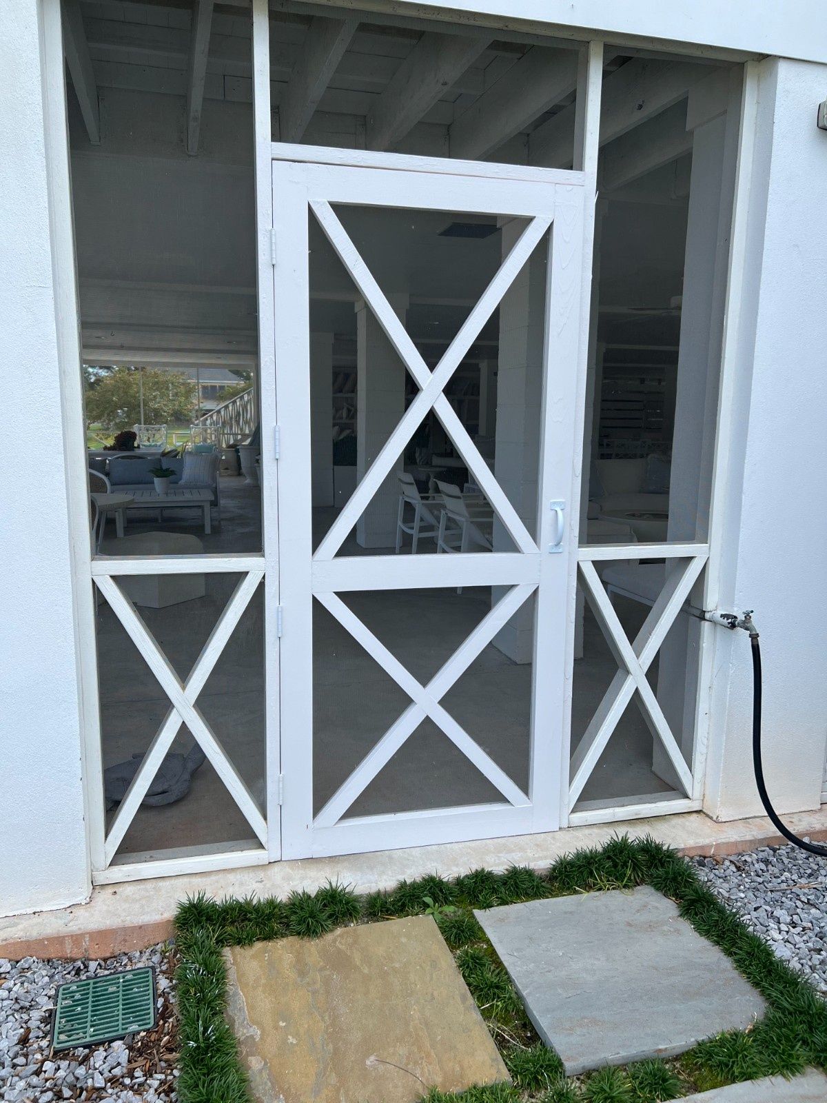 White cross-braced porch gate in front of a screened patio, with stepping stones and grass below.