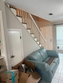 Living room with teal couch, staircase, white doors, and boxes in the corner