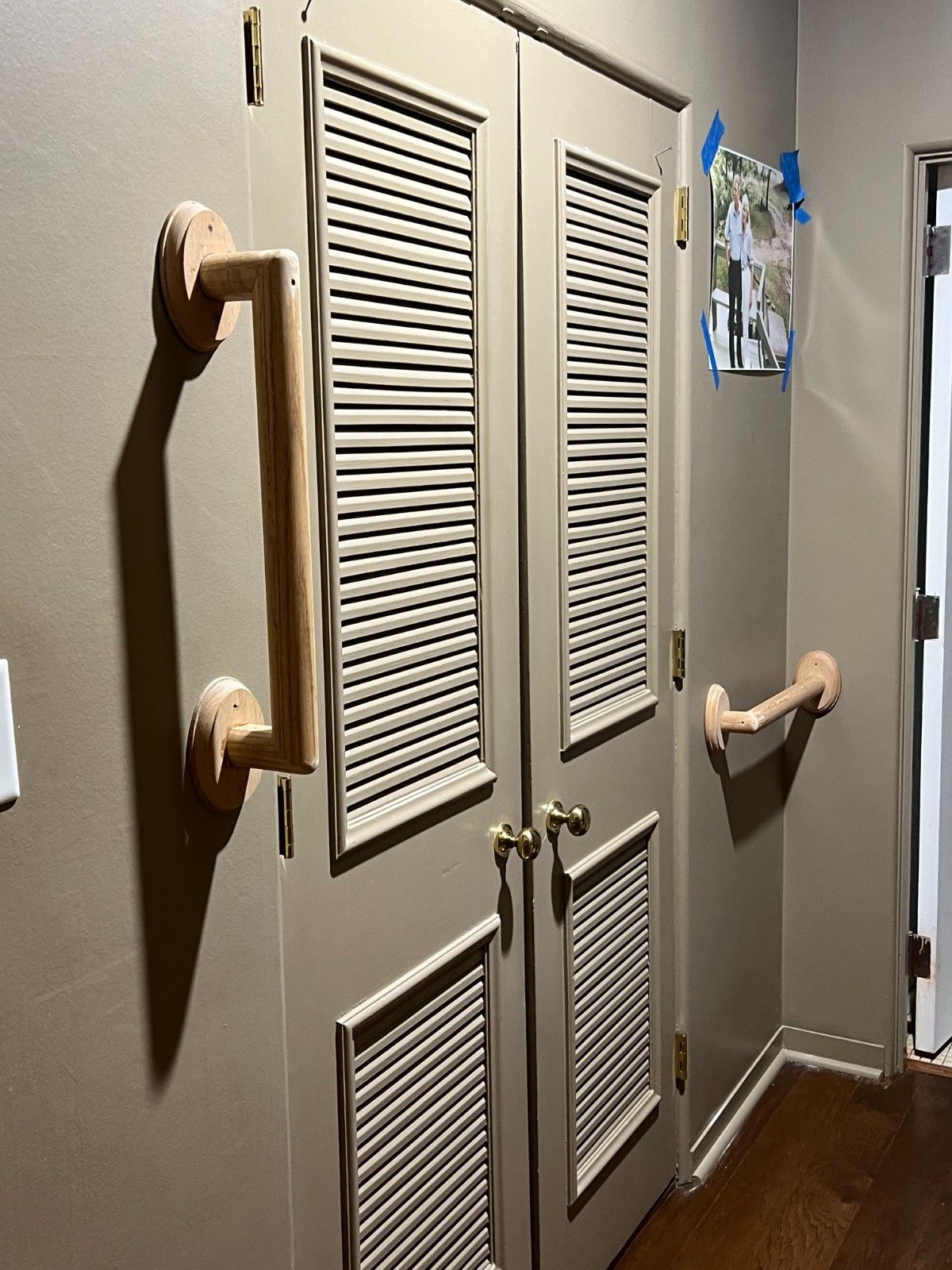 Gray louvered closet doors with multiple beige grab bars mounted around them in a hallway