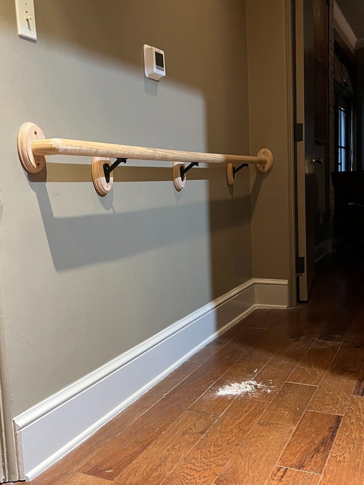 Wooden wall-mounted handrail in a hallway with gray walls and hardwood floor, angled for support.