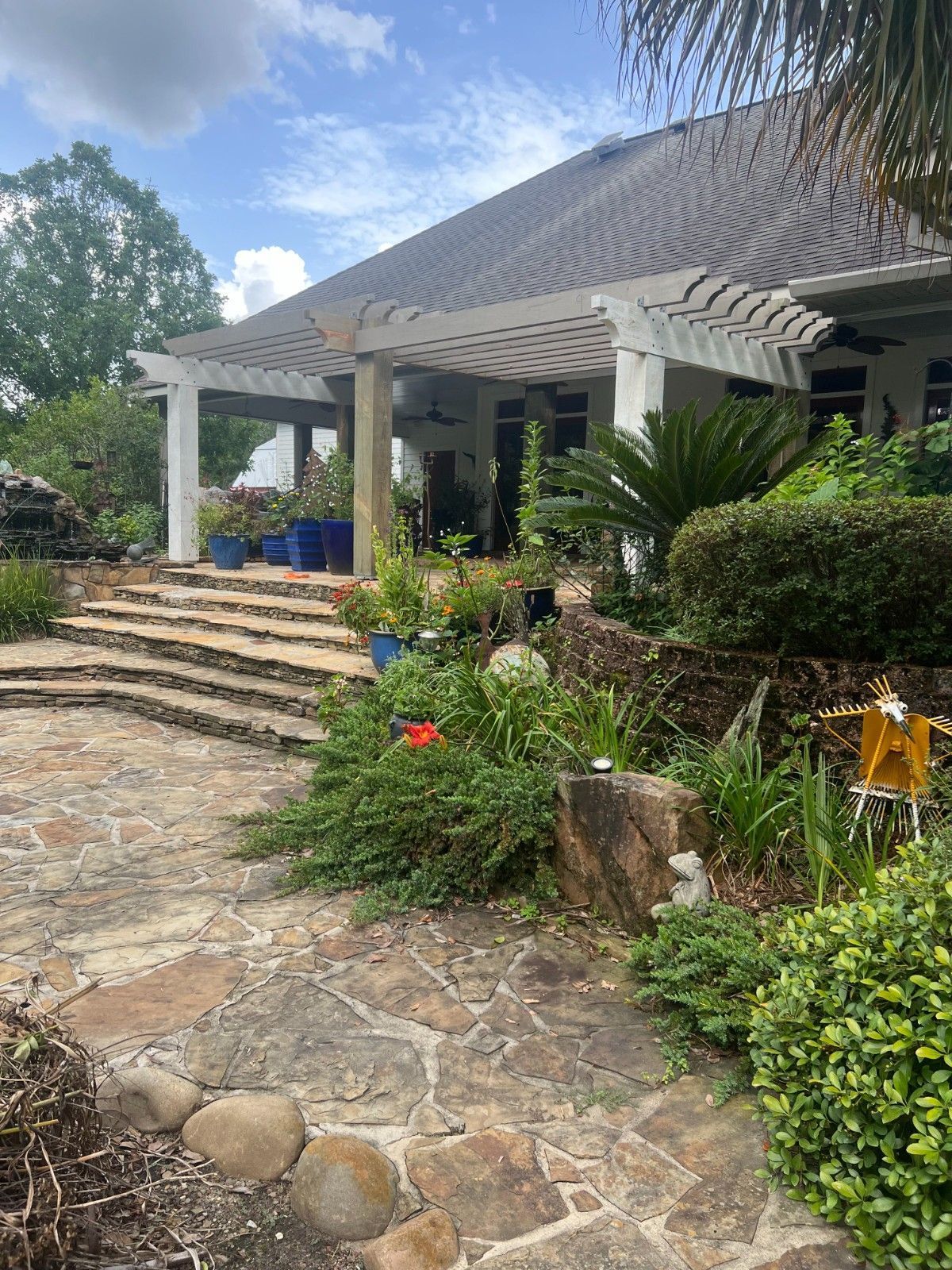 Stone path leads to a white house with steps, porch columns, and lush tropical landscaping.