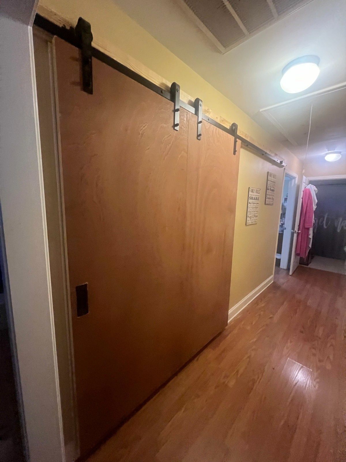 Hallway with large wooden sliding doors on a track, hardwood floor, and hanging clothes in the distance