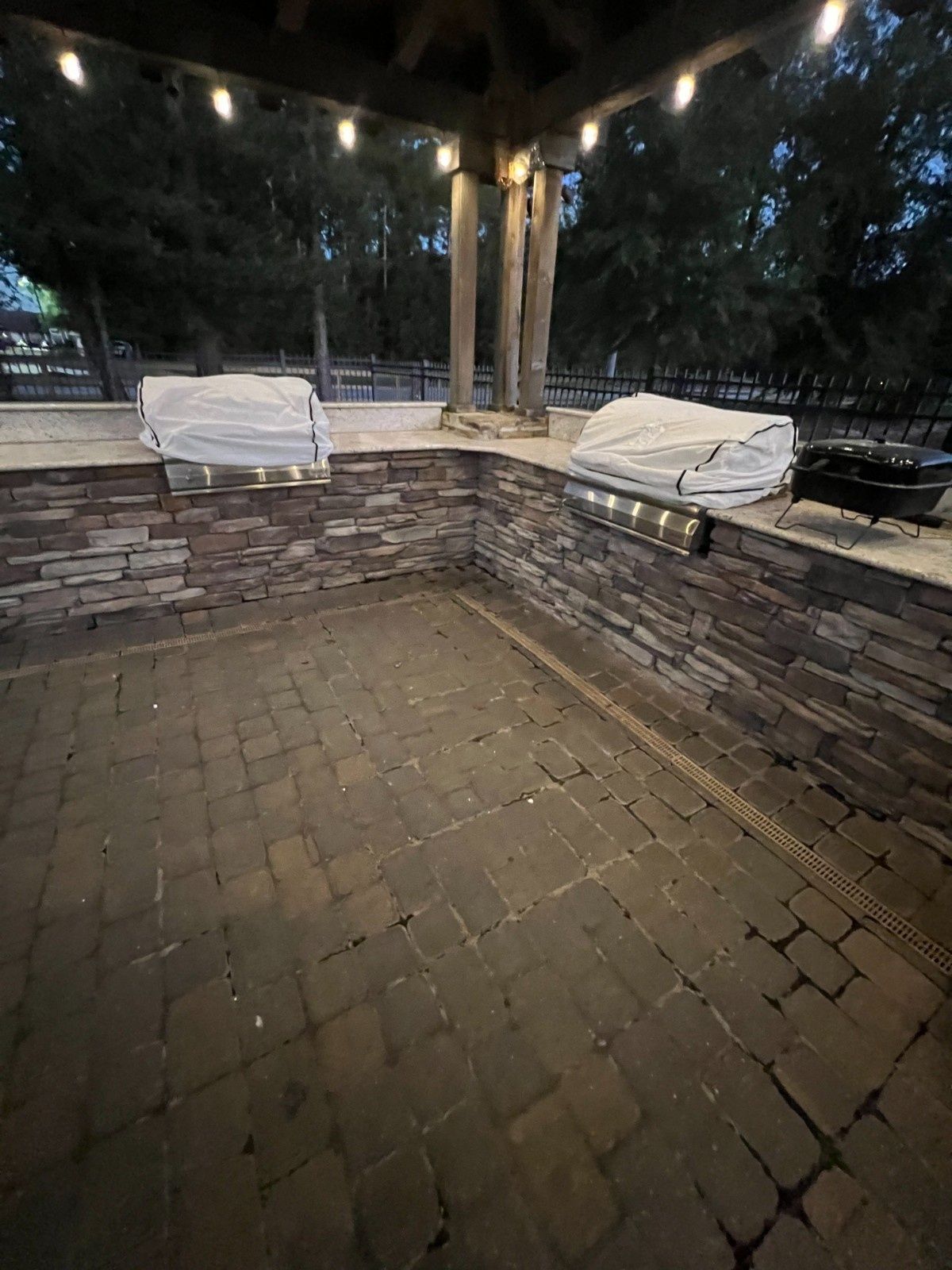 Brick patio seating area under a wooden pergola with string lights and covered cushions at dusk