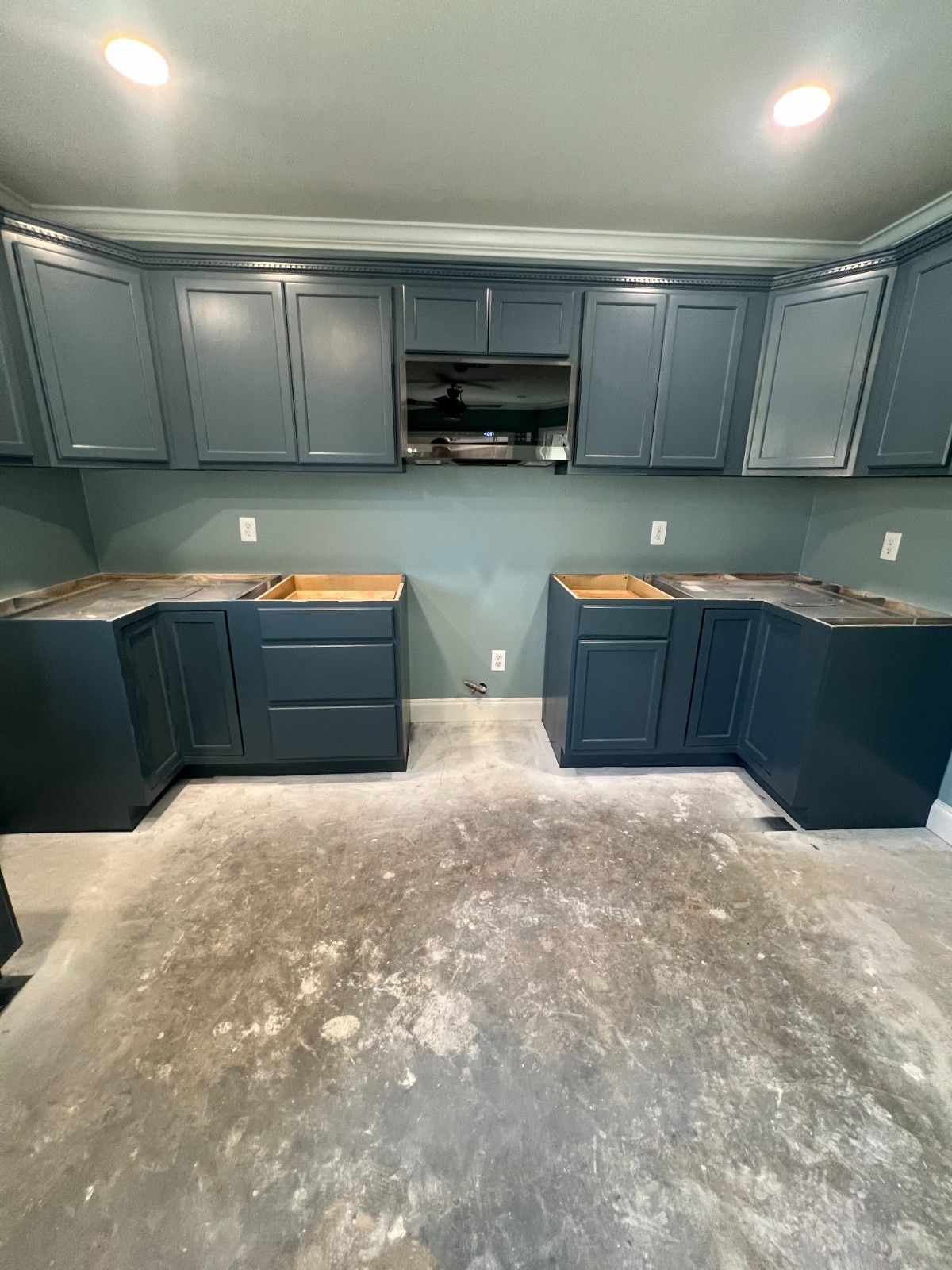 Empty kitchen with dark blue cabinets, teal walls, and unfinished concrete floor.