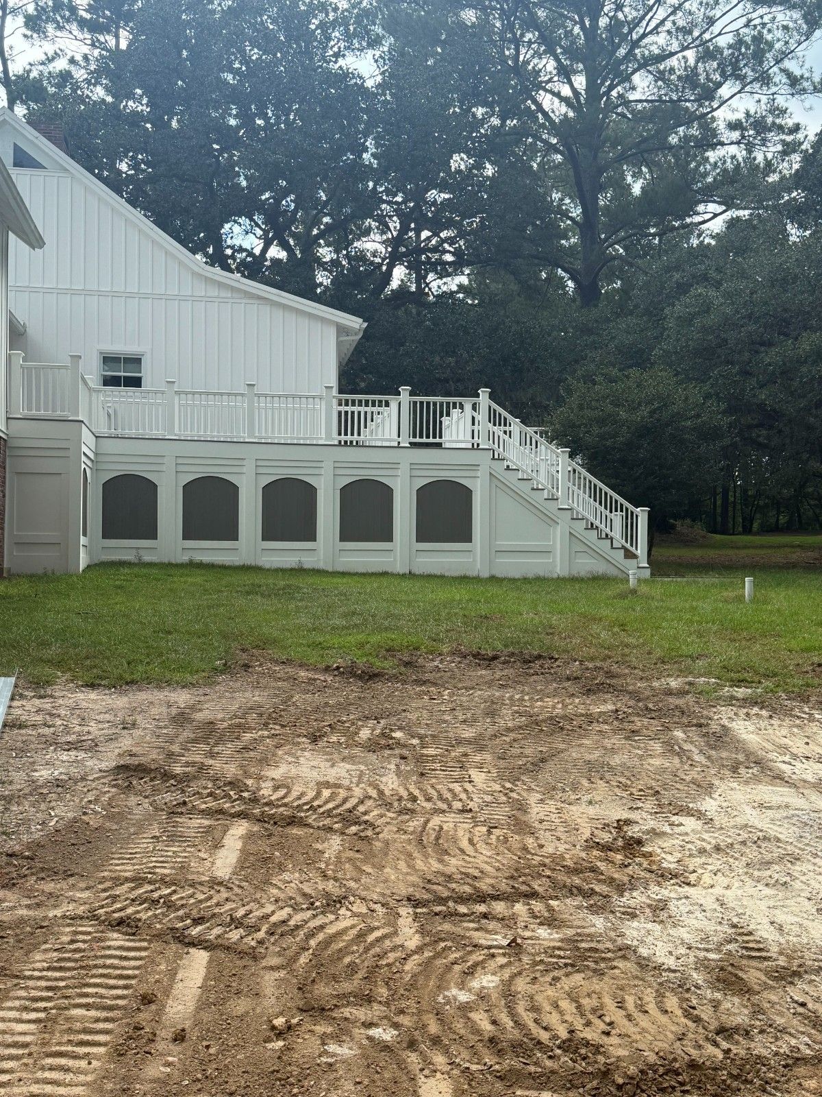 White house with deck and stairs beside a muddy, graded yard and trees.