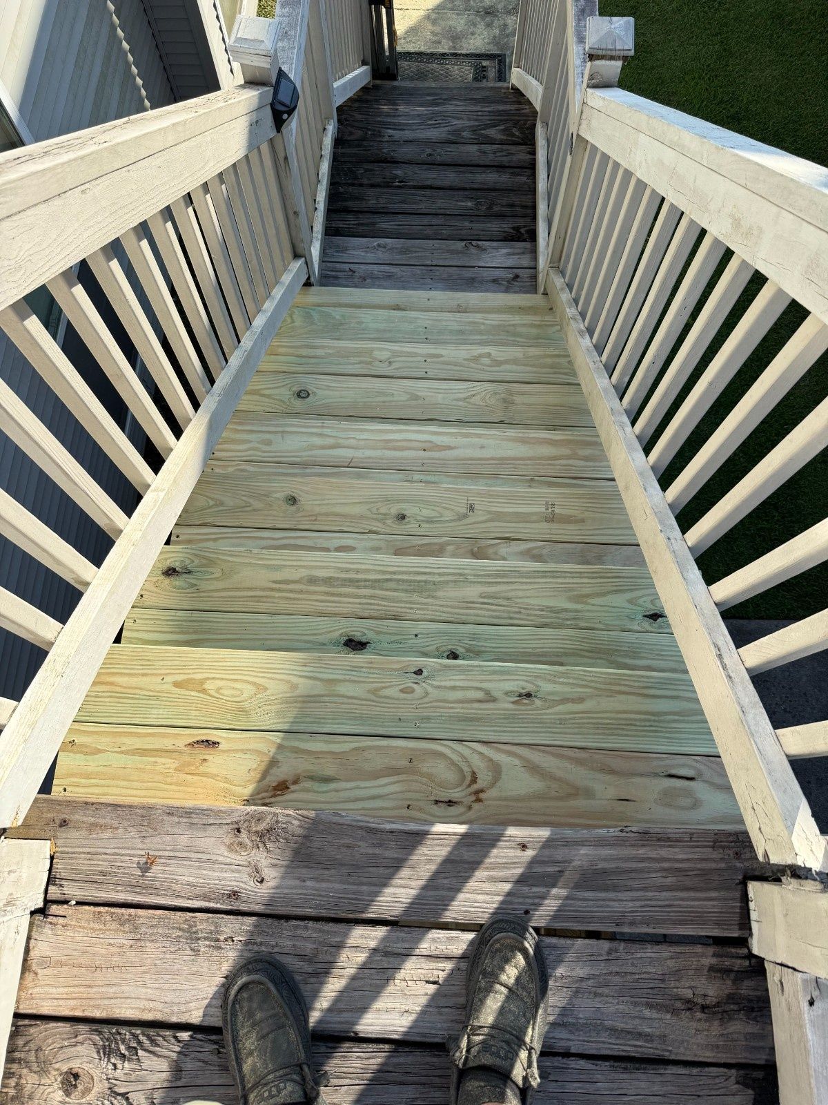 Wooden walkway with railings leading up to stairs, viewed from someone standing at the bottom.