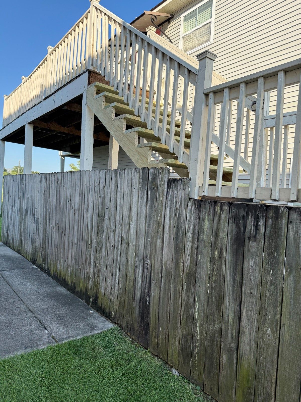 Wooden outdoor staircase and deck beside a weathered privacy fence and house exterior.